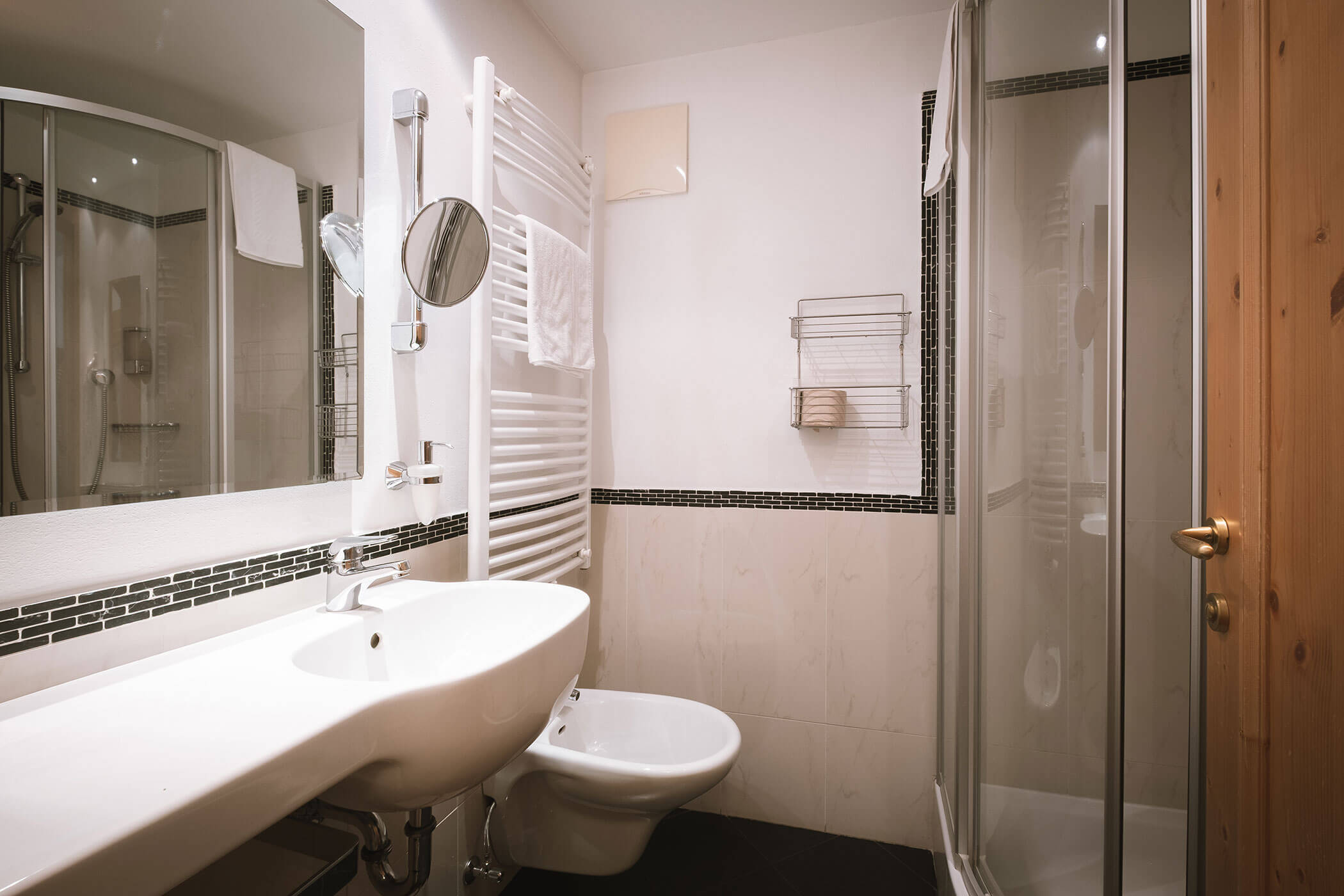 Bagno moderno con lavandino, bidet, doccia in vetro, portasciugamani e grande specchio a parete. - Hotel Innerhofer