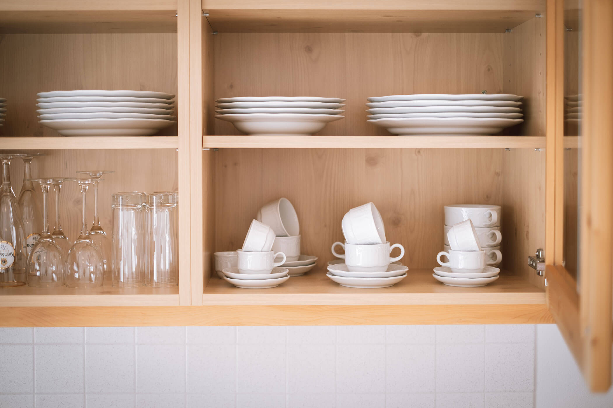 Wooden kitchen shelves with neatly stacked white plates, bowls, cups, and glasses. - Hotel Innerhofer
