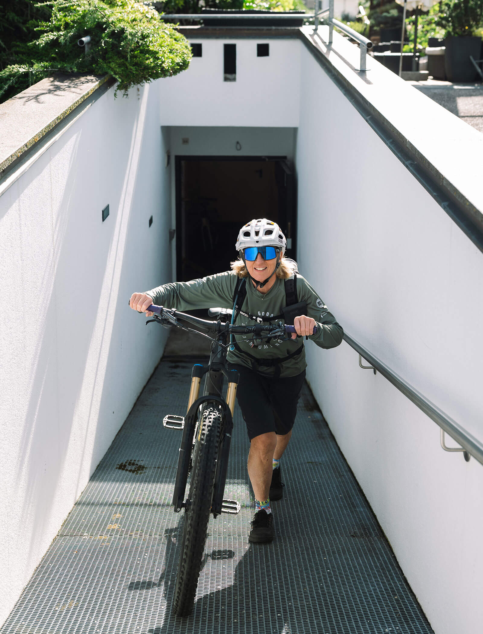 Persona con casco e occhiali da sole che spinge una mountain bike su una rampa da un passaggio sotterraneo. - Hotel Innerhofer