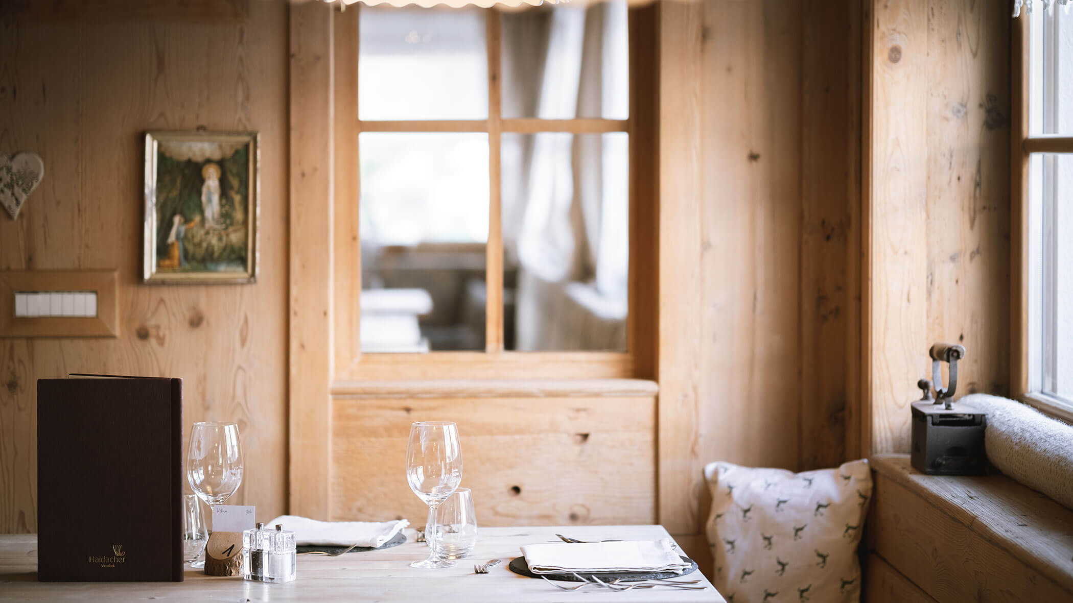 Elegant table for two set with wine glasses in a cozy, wood-paneled restaurant with soft natural light. - Hotel Innerhofer