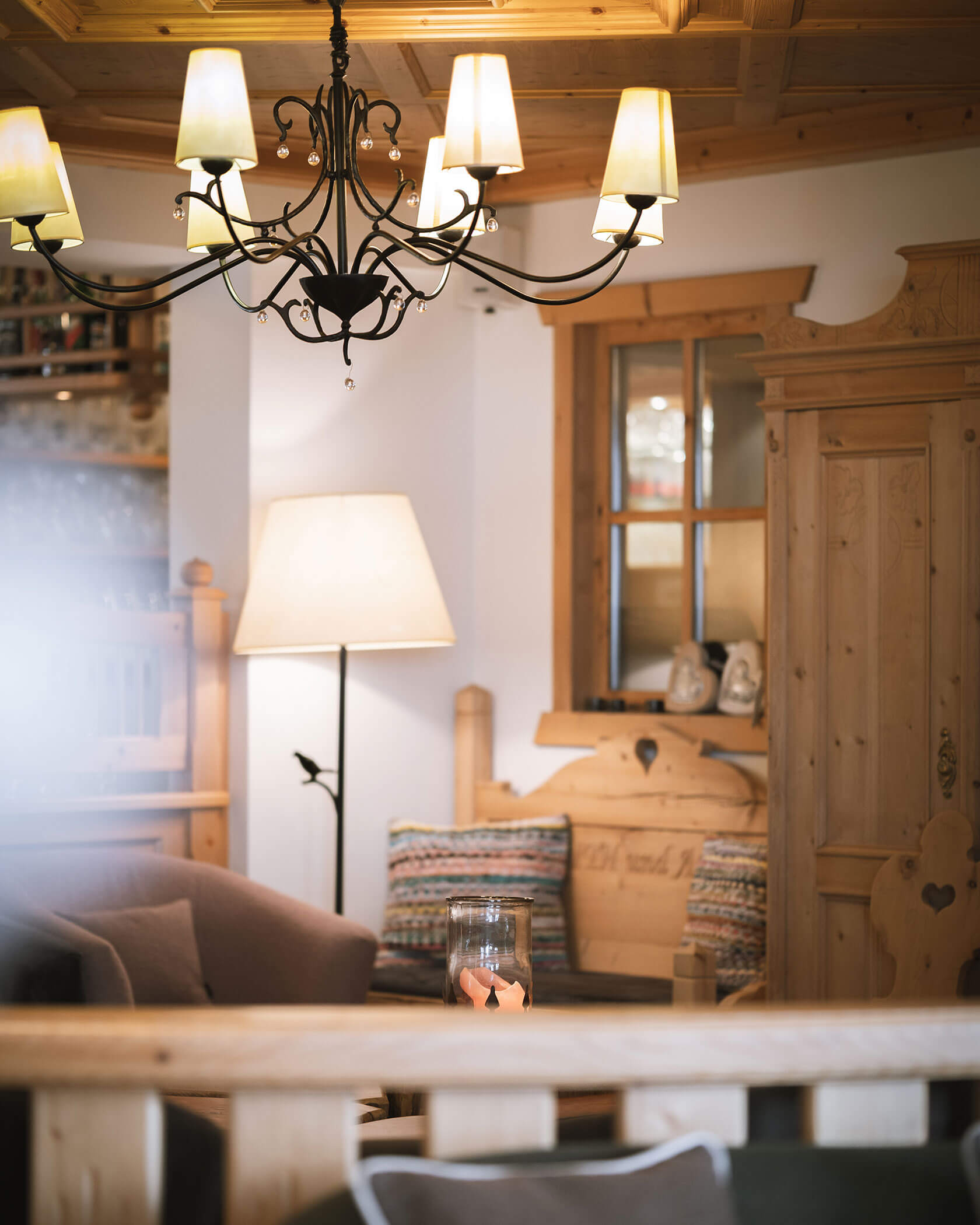 Cozy living room with wooden furniture, soft lighting, a chandelier, and a large floor lamp. - Hotel Innerhofer
