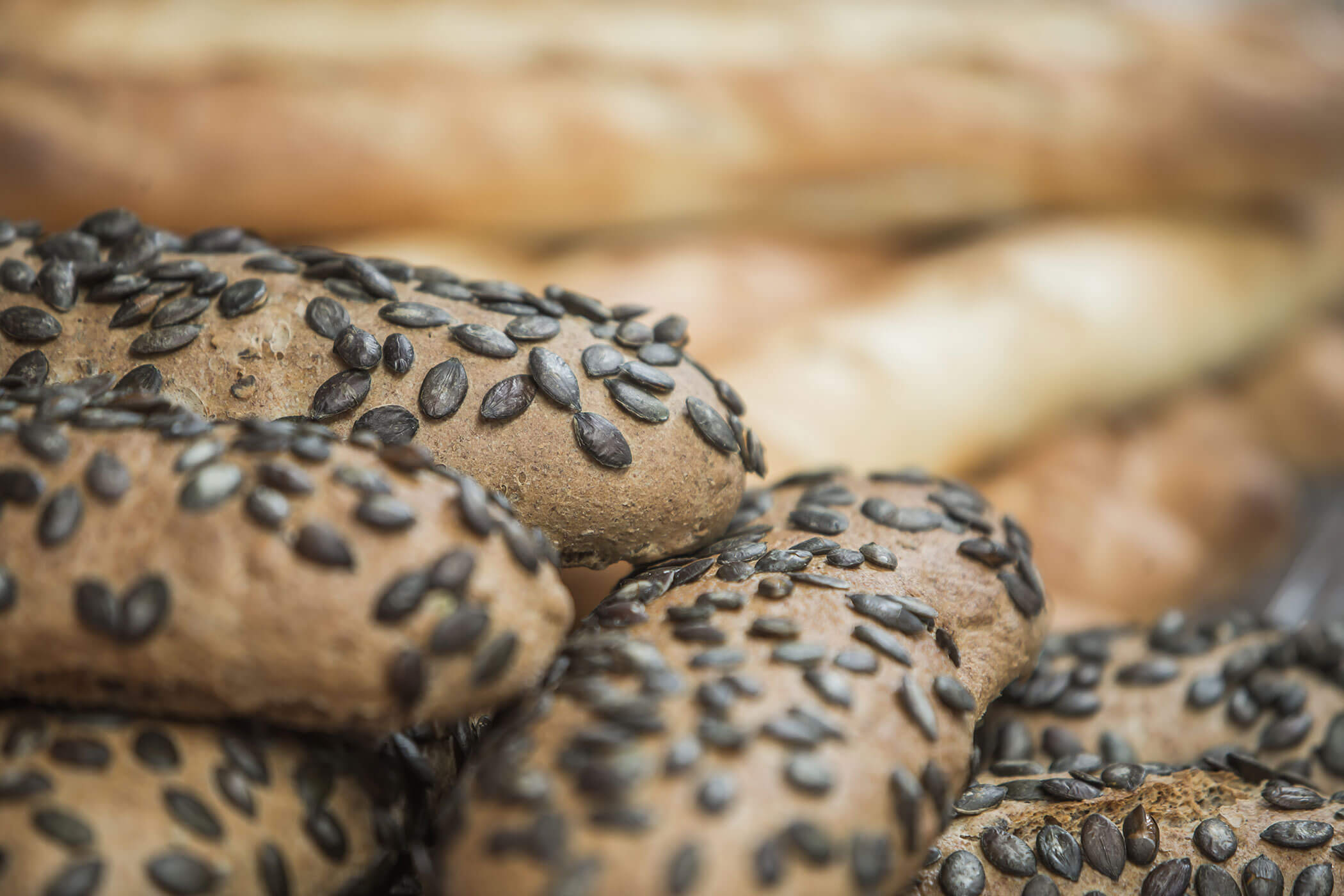 Nahaufnahme von braunen, mit Sonnenblumenkernen belegten Brotstangen, im Hintergrund sind einfache Brotstangen zu sehen. - Hotel Innerhofer
