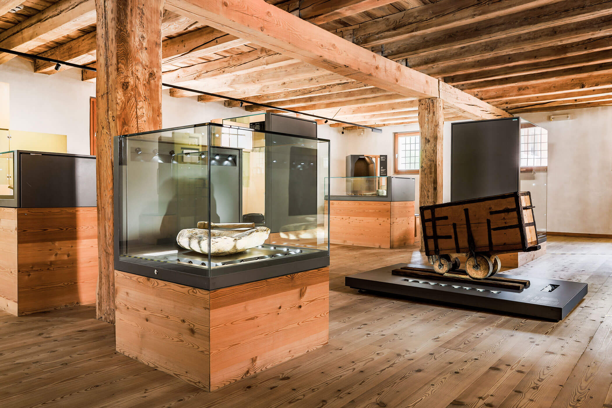Museum exhibit with wooden beams, glass display cases, and historical artifacts on wooden floors. - Hotel Innerhofer