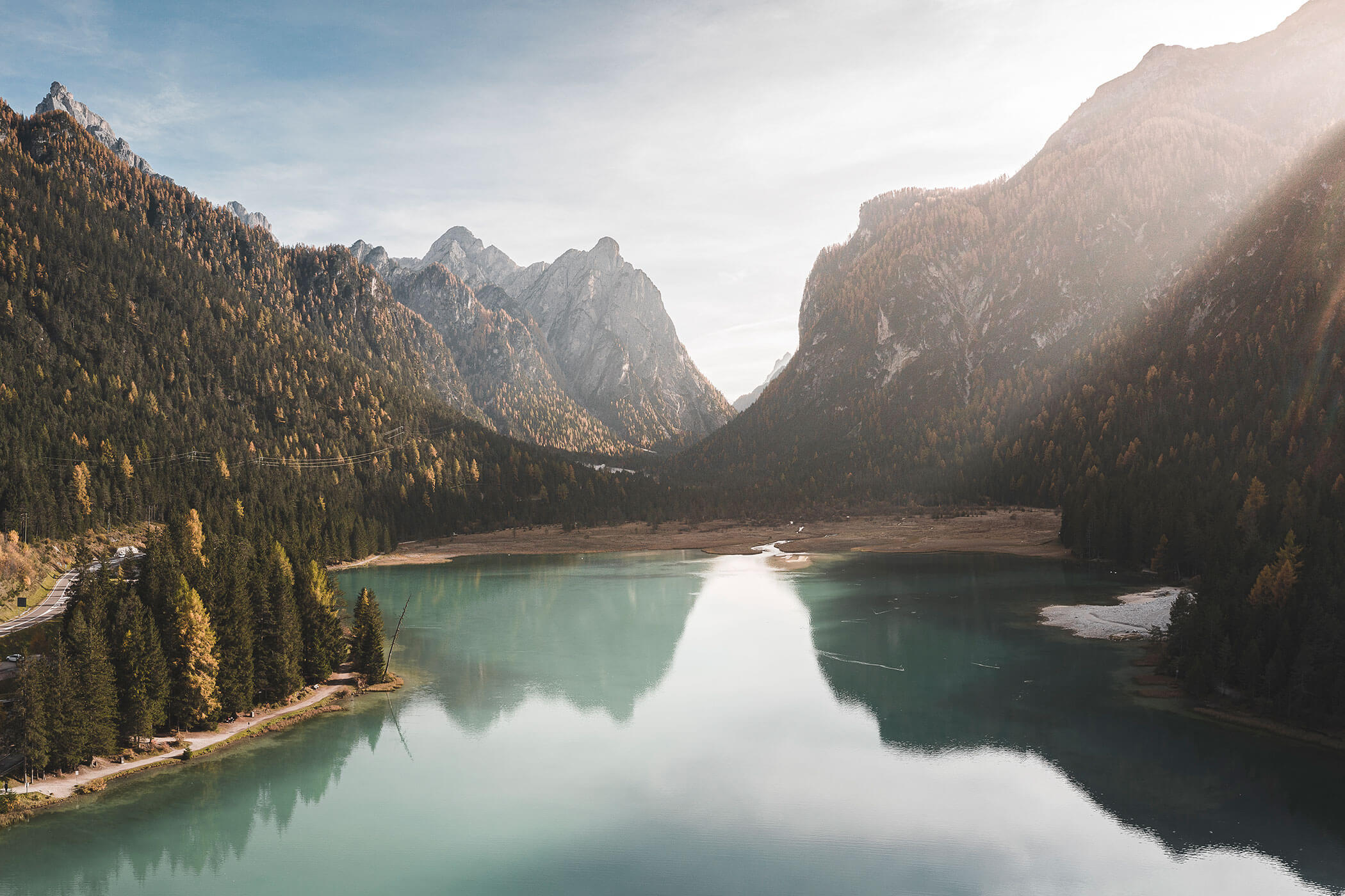 Serene mountain lake with calm water, surrounded by forested peaks under a partly cloudy sky. - Hotel Innerhofer