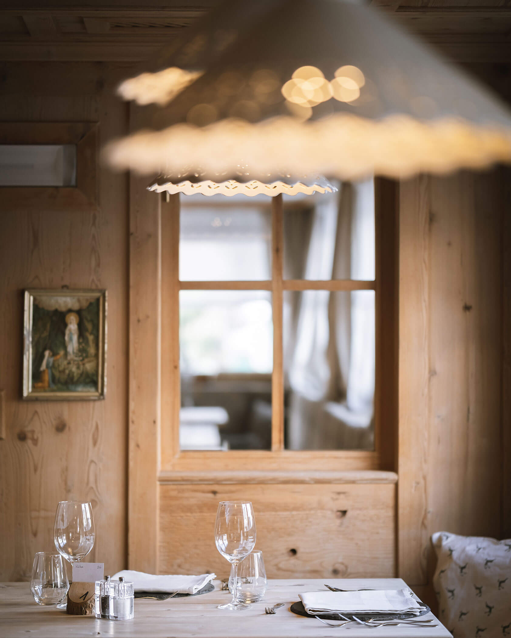 Eine gemütliche Essecke aus Holz mit gedecktem Tisch, Weingläsern und einer großen Hängelampe darüber. - Hotel Innerhofer