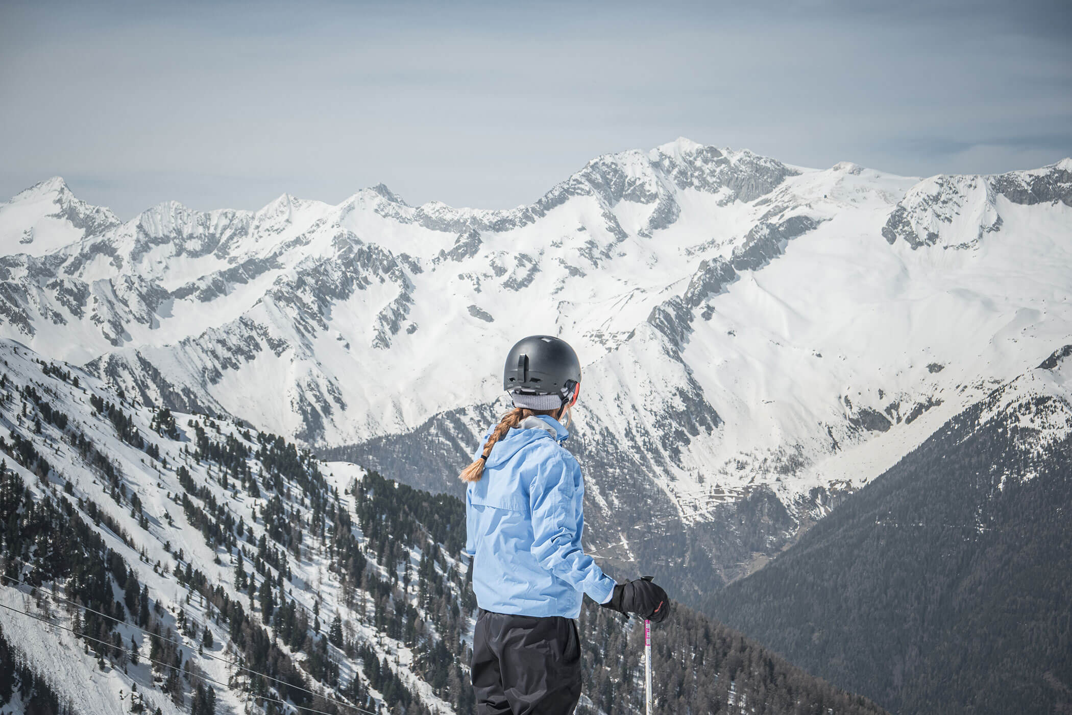 Person in blue jacket and helmet looks at snowy mountains while skiing on a bright winter day. - Hotel Innerhofer
