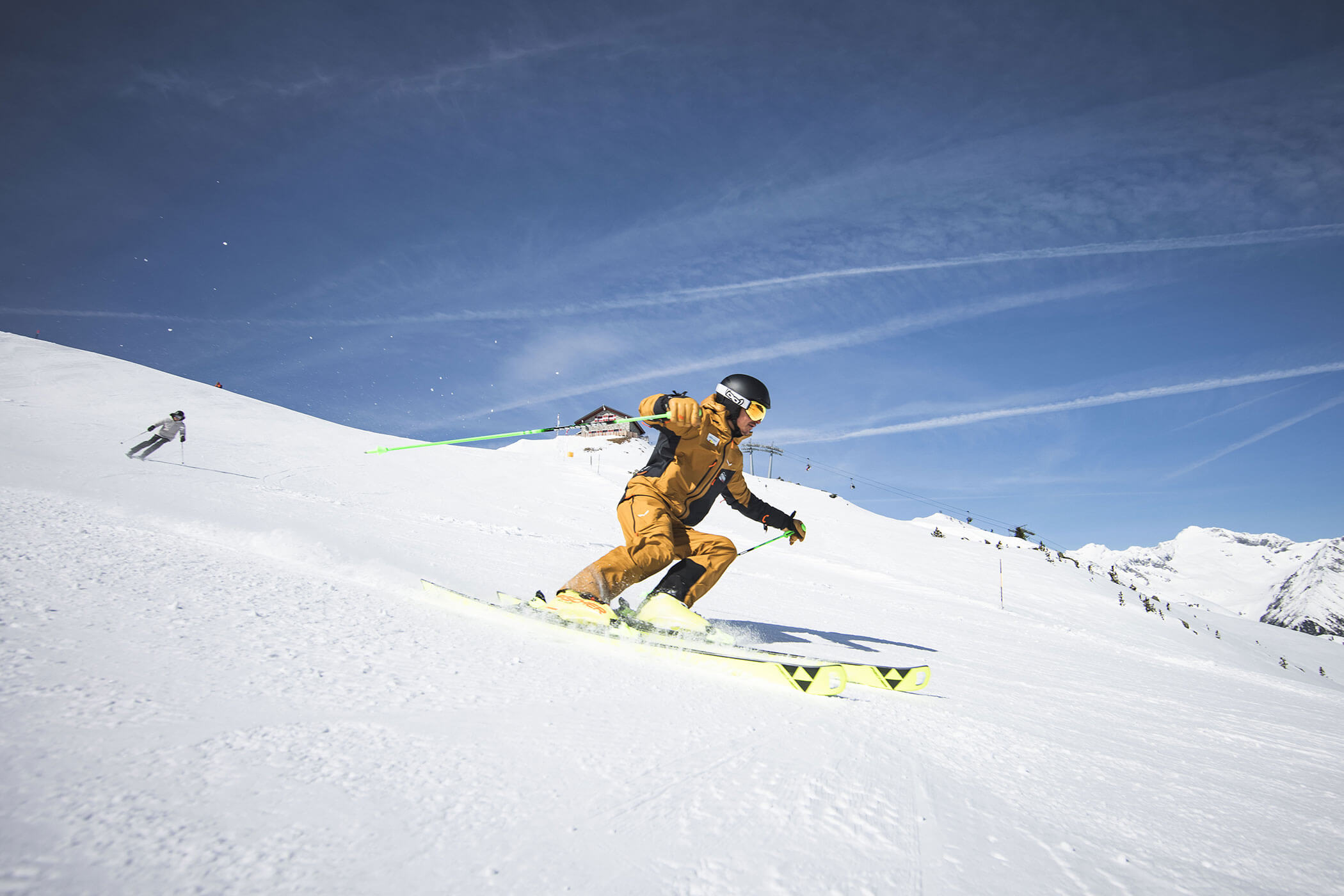 A skier in a yellow suit speeds downhill on a snowy slope under a clear blue sky. - Hotel Innerhofer
