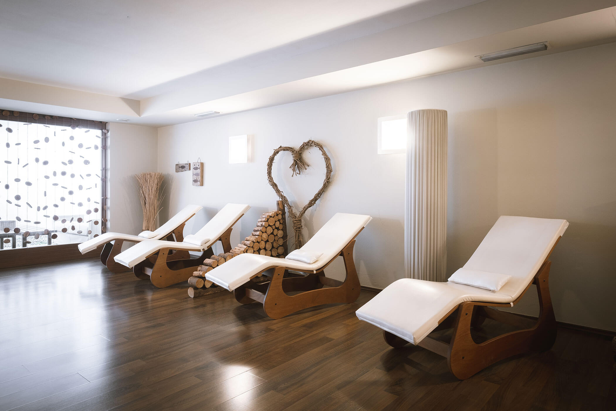 Quattro moderne poltrone lounge con cuscini bianchi in una sala spa serena e illuminata da luci soffuse, con pavimenti e decorazioni in legno. - Hotel Innerhofer