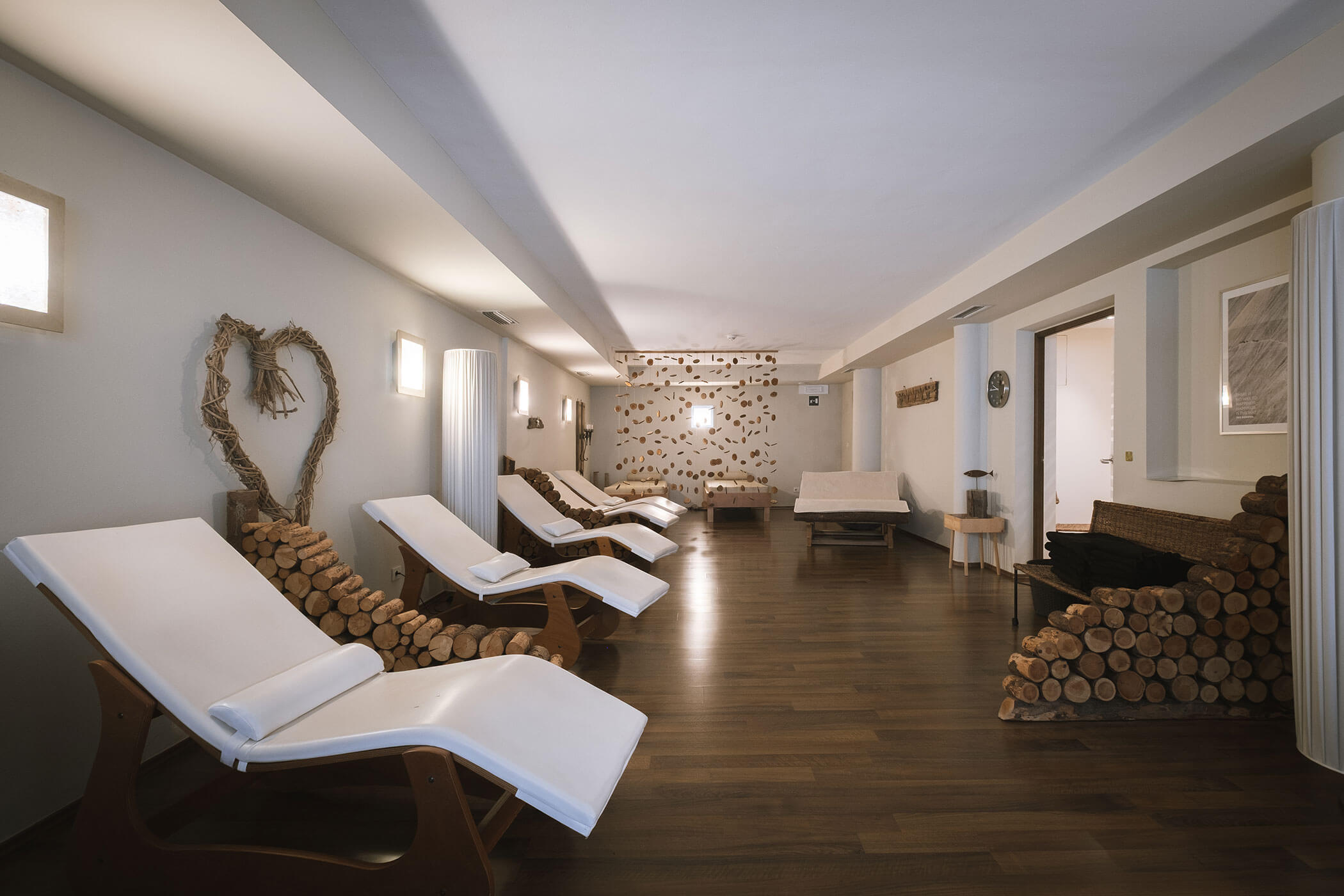 Moderna spa lounge con poltrone bianche reclinabili, decorazioni in legno e illuminazione d'ambiente su un pavimento in legno lucido. - Hotel Innerhofer