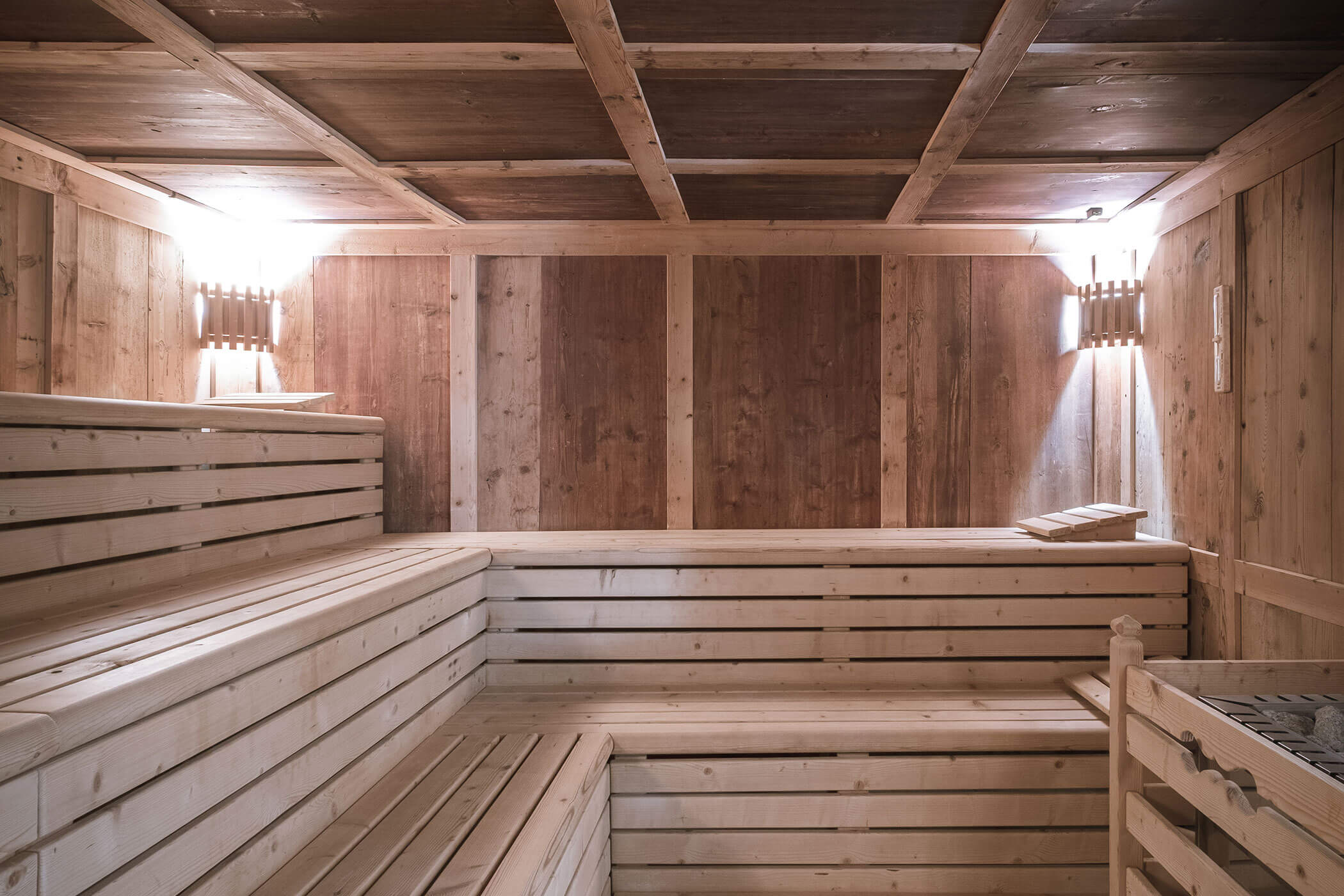 Interno della sauna in legno con panche, illuminazione calda a parete e poggiatesta sulla panca superiore. - Hotel Innerhofer