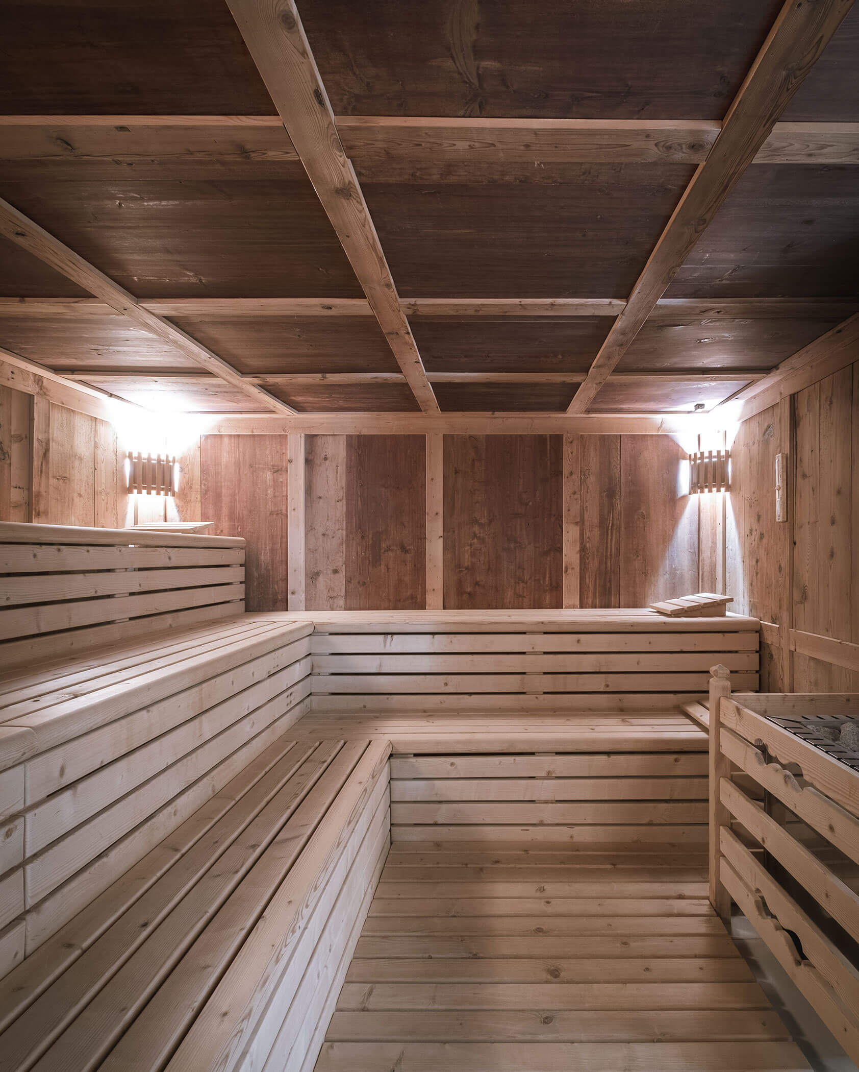 Wood-paneled sauna interior with tiered benches, soft lighting, and a towel on the top bench. - Hotel Innerhofer